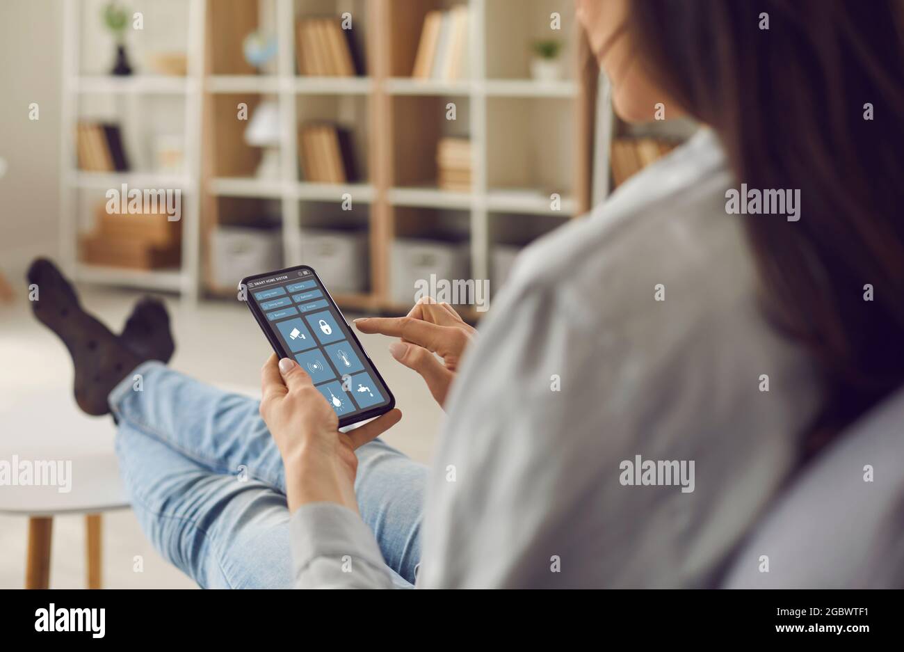 Frau steuert das System ihres modernen Smart House über eine App auf ihrem Smartphone Stockfoto