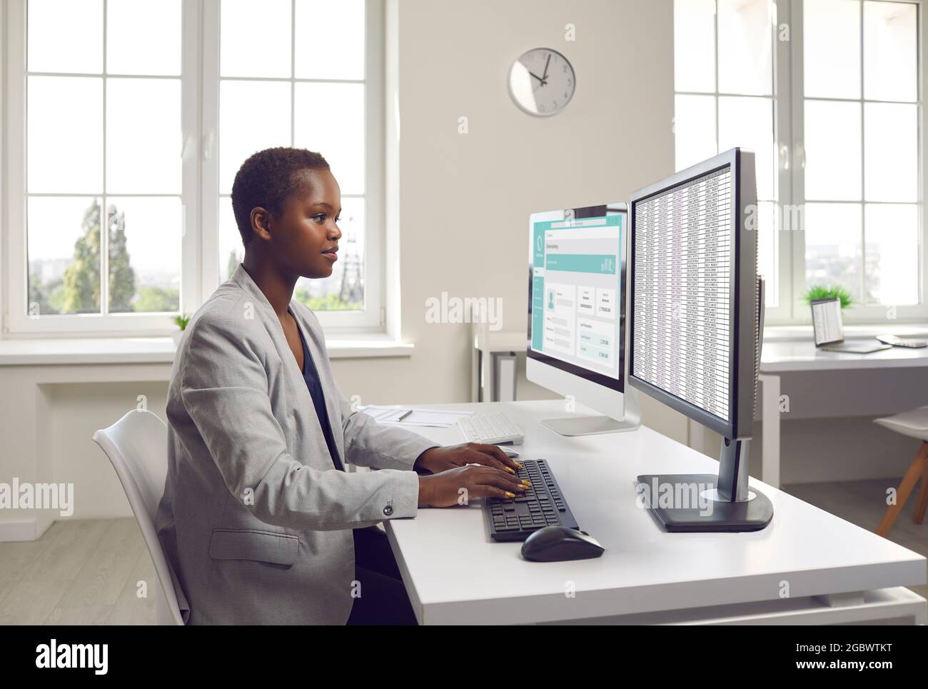 Geschäftsfrau oder Buchhalterin, die mit Finanzdokumenten auf zwei Bürocomputern arbeitet Stockfoto
