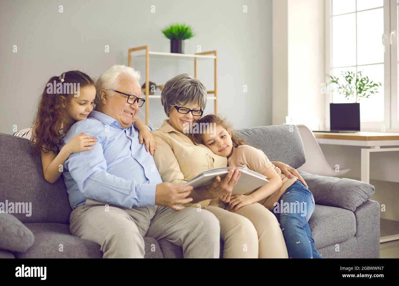 Glückliche Großeltern mit zwei Enkelkindern stöbern in Familienfotos und teilen glückliche Erinnerungen. Stockfoto