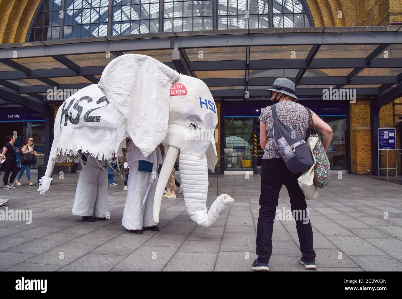 London, Großbritannien. August 2021. Demonstranten, die ein weißes Elefantenkostüm "HS2" tragen, werden während des Stop-HS2-Protests von einem Mitdemonstrator vor den Bahnhof geführt.Aktivisten versammelten sich vor der King's Cross Station, um gegen das neue Hochgeschwindigkeits-2-Eisenbahnsystem (HS2) zu protestieren. Die Umweltschützer sagen, dass sie „ökologisch verheerend“ sein und den Steuerzahler £170 Milliarden kosten werden. (Foto: Vuk Valcic/SOPA Images/Sipa USA) Quelle: SIPA USA/Alamy Live News Stockfoto