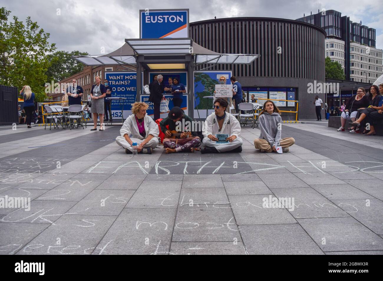 London, Großbritannien. August 2021. Während des Stop HS2-Protests sitzen Demonstranten auf dem Boden, bedeckt mit kalkgeschriebenen Anti-HS2-Slogans, neben einem Euston HS2-Informationsstand.Aktivisten versammelten sich vor der King's Cross Station, um gegen das neue Hochgeschwindigkeits-2-Eisenbahnsystem (HS2) zu protestieren. Die Umweltschützer sagen, dass sie „ökologisch verheerend“ sein und den Steuerzahler £170 Milliarden kosten werden. (Foto: Vuk Valcic/SOPA Images/Sipa USA) Quelle: SIPA USA/Alamy Live News Stockfoto