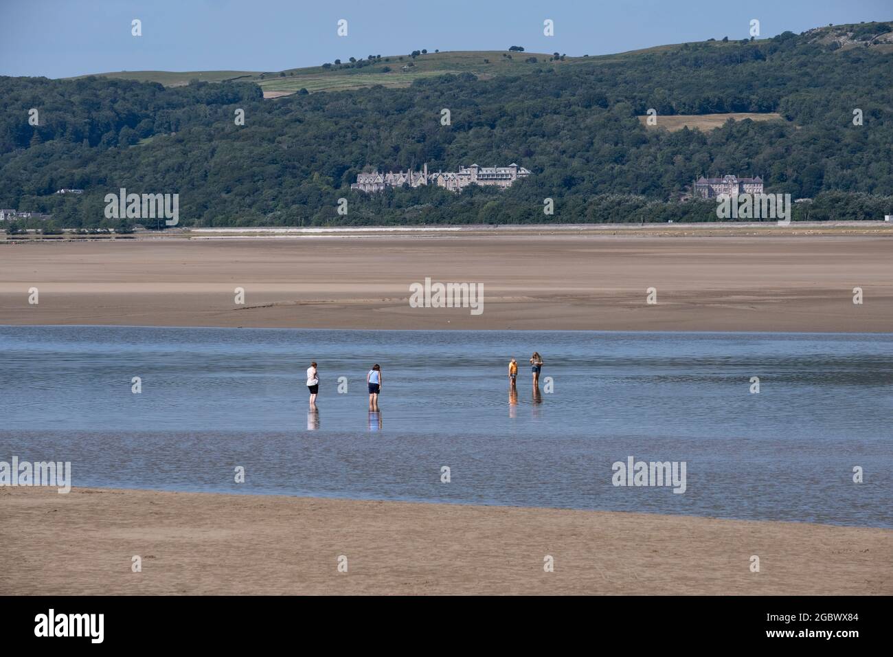 Urlauber in Arnside in Lancashire, England, während der Sommerferien, während der Ozean vor dem Wasser steht und zwischen zwei Sandstränden einen Streifen Wasser hinterlässt. Stockfoto
