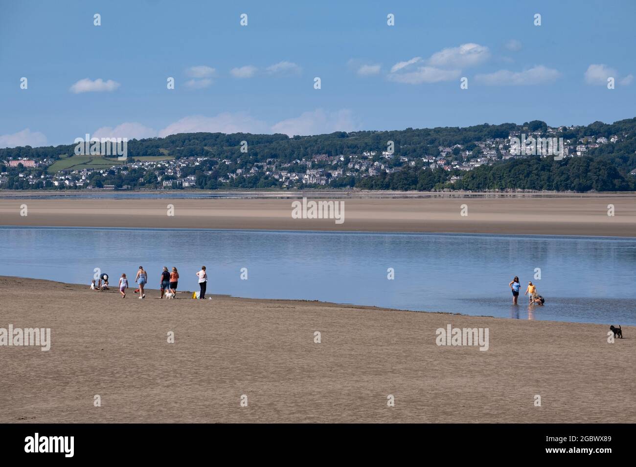 Urlauber in Arnside in Lancashire, England, während der Sommerferien, während der Ozean vor dem Wasser steht und zwischen zwei Sandstränden einen Streifen Wasser hinterlässt. Stockfoto