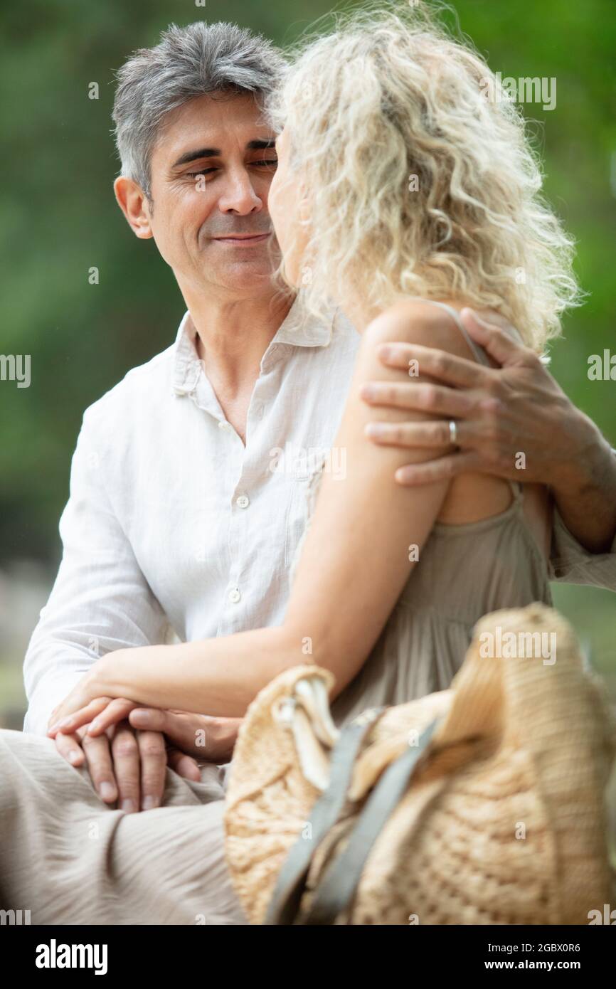 Ein älterer Mann umarmt seine Frau, die auf der Bank steht Stockfoto