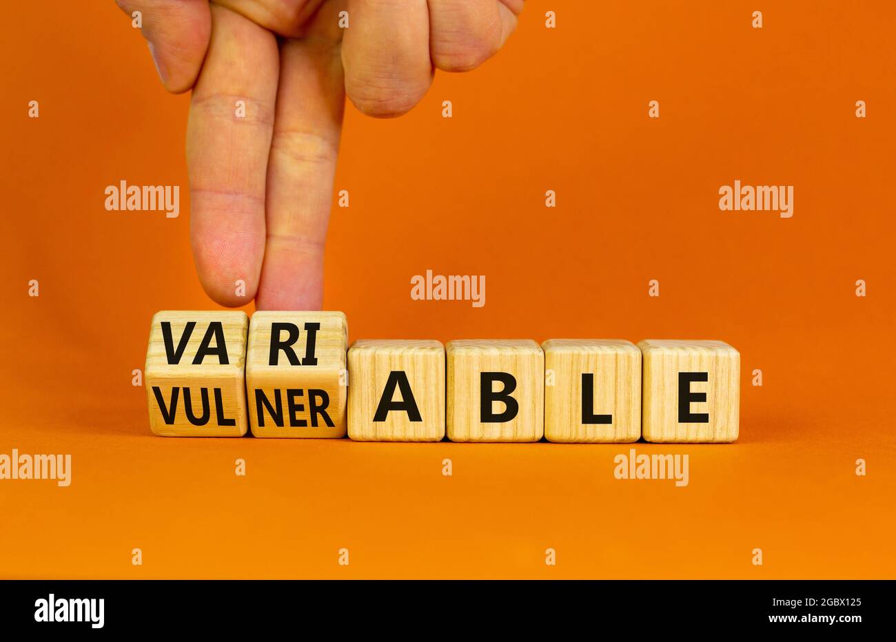 Verletzlich oder variables Symbol. Geschäftsmann dreht Holzwürfel und ändert das Wort anfällig für variable. Schöner orangefarbener Hintergrund, Kopierbereich. Bu Stockfoto