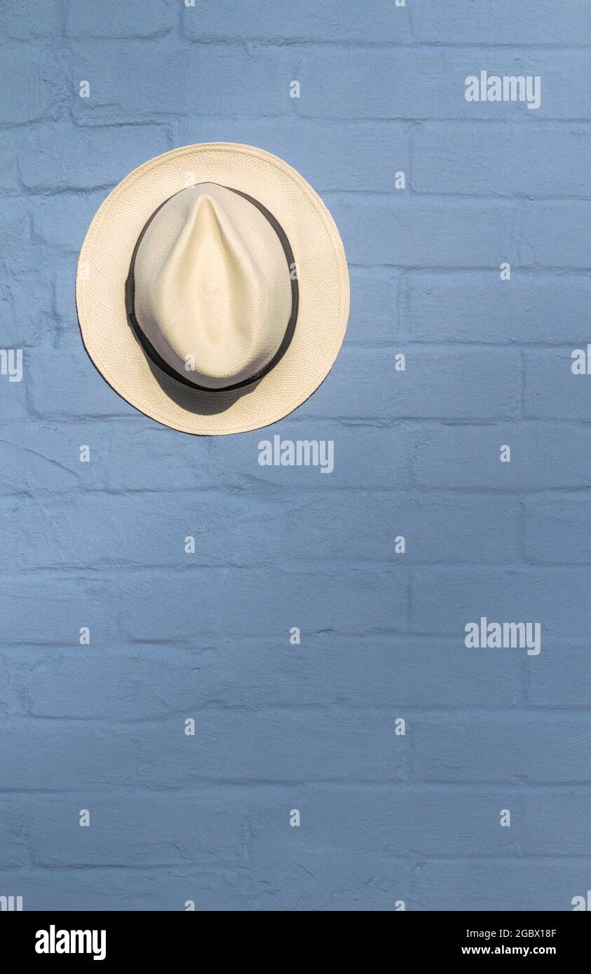 Einzelner Panama Strohhut, der an einer blau gemalten Ziegelwand aufgehängt wird, England, Großbritannien Stockfoto
