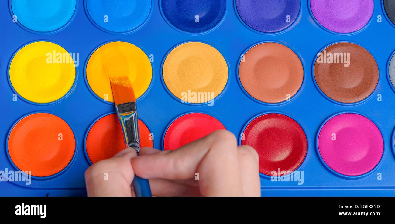 Ein Satz Aquarellfarben und ein Pinsel zum Zeichnen von Nahaufnahme. Kinderhand mit einem Pinsel. Selektiver Fokus. Stockfoto