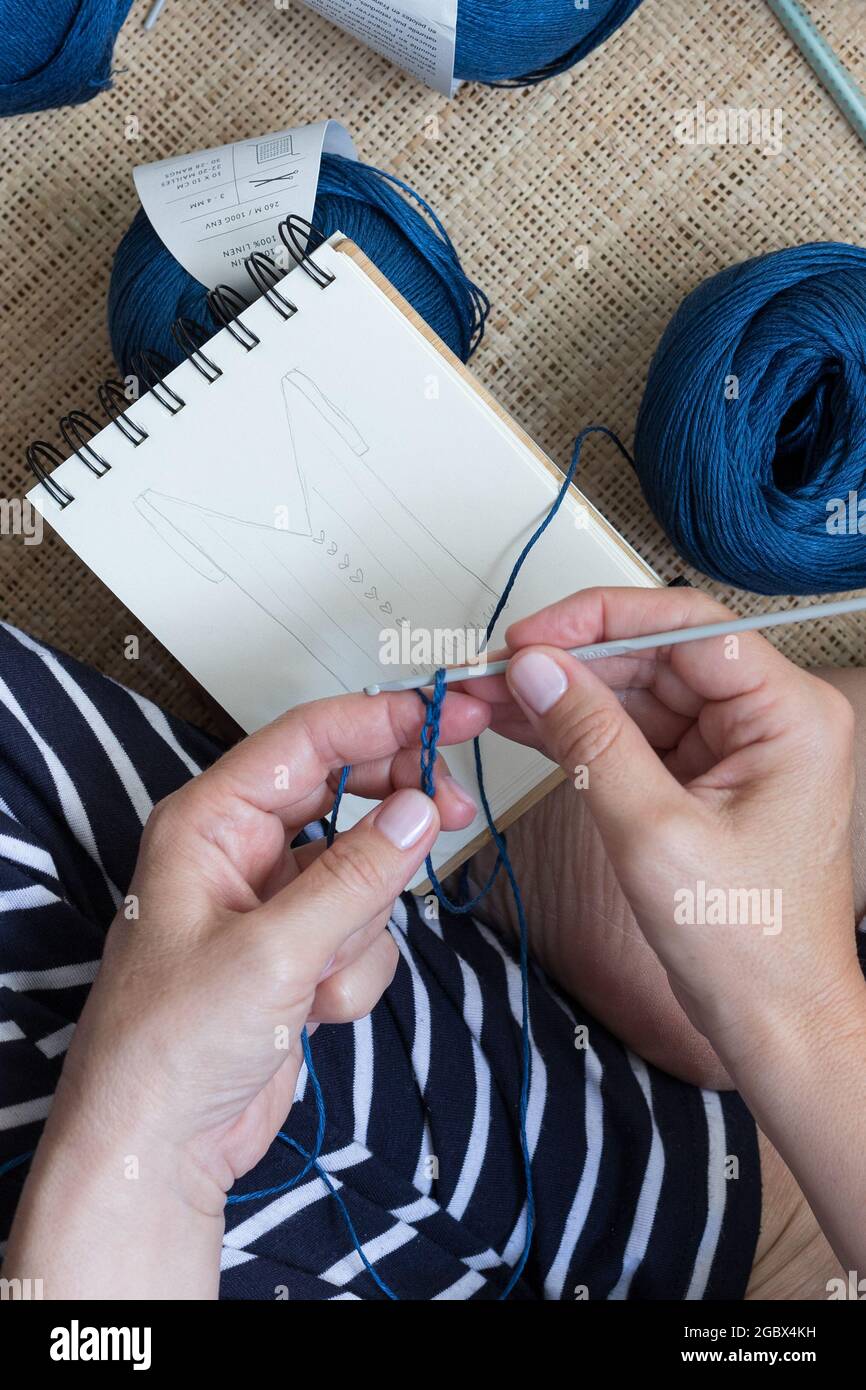 Nahaufnahme einer Frau, die einen blauen Leinenstich über ein handgezeichnetes Design häket. Stockfoto