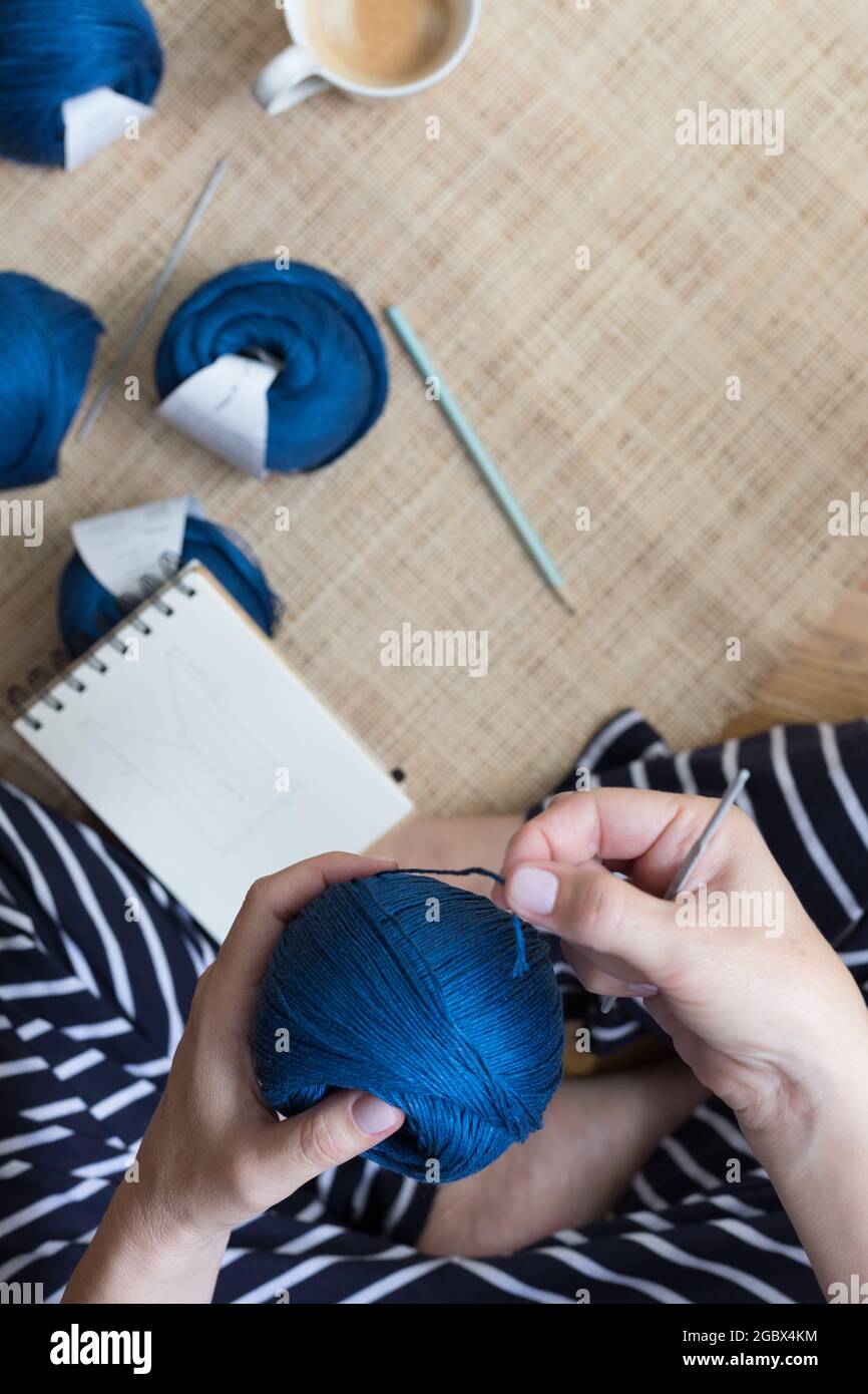Sitzende Frau mit gestreiftem Kleid und einem blauen Leinengarn zum Häkeln. Stockfoto