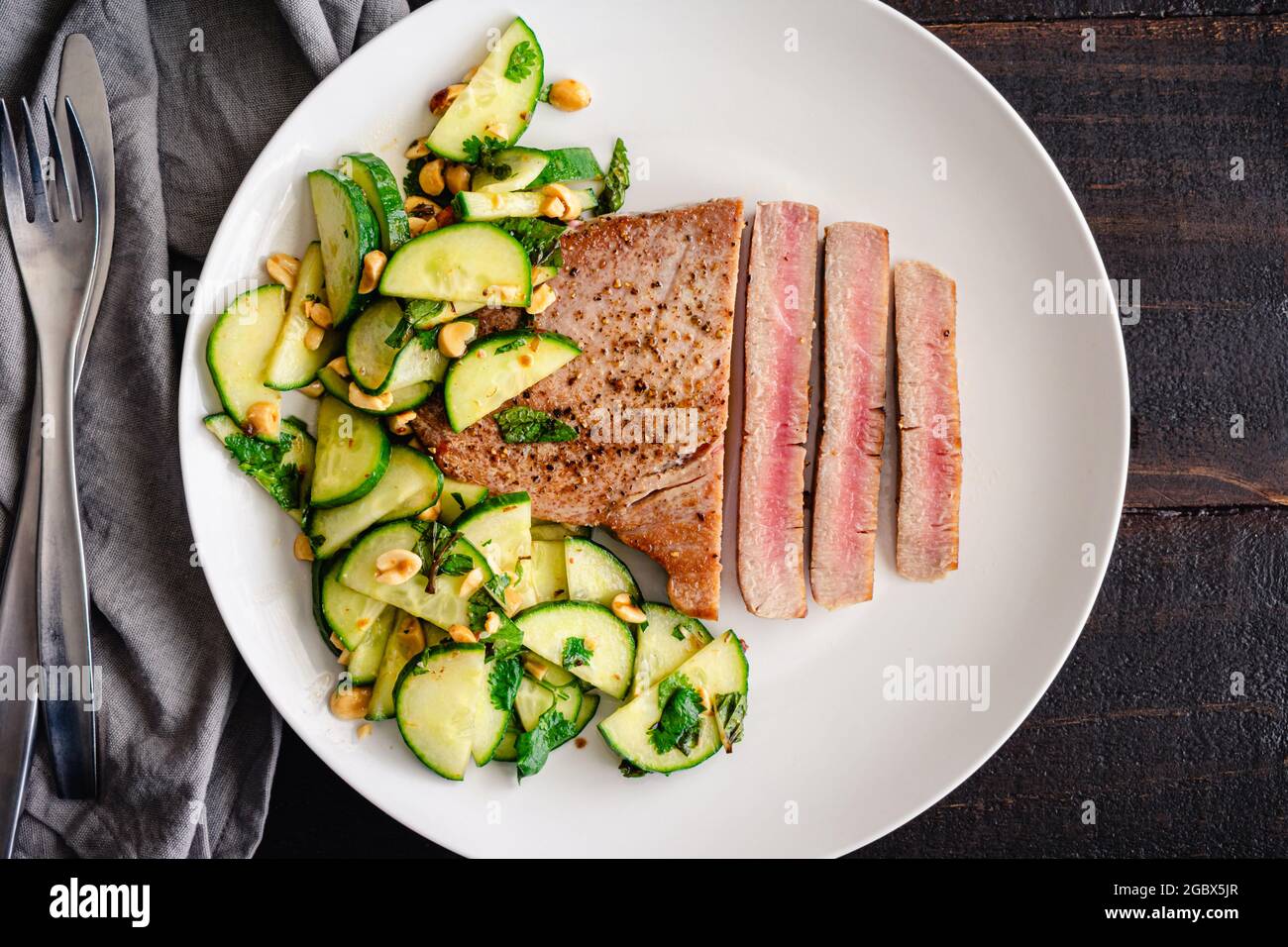 Thunfischsteak mit Gurken-Erdnusssalat: Seltenes Fischfilet, serviert mit Gurken- und Erdnusssalat als Beilage Stockfoto