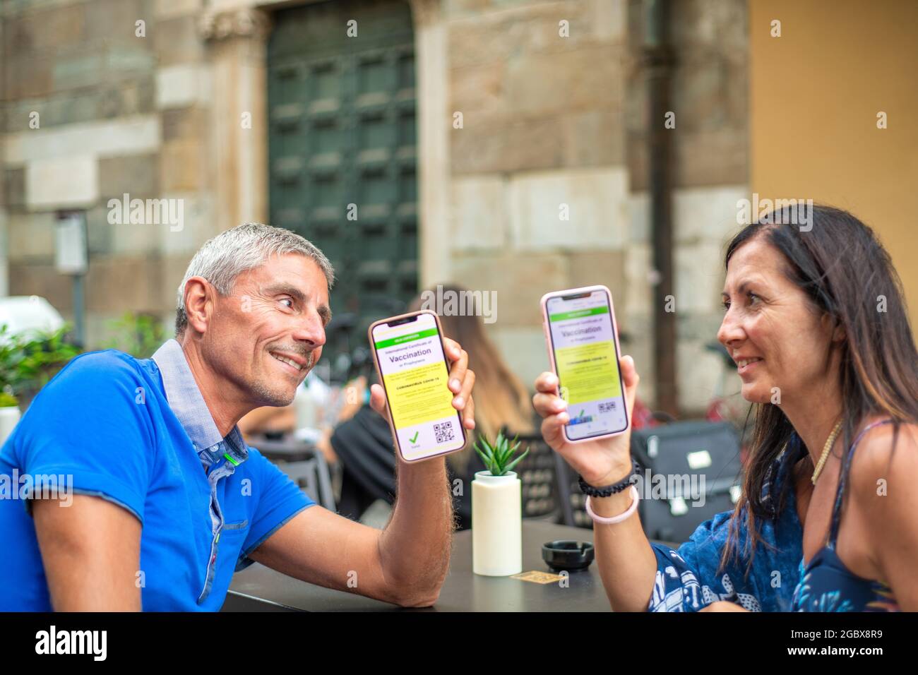 Ein glückliches Paar saß an einem Restauranttisch mit einem grünen Pass. Mann und Frau sind bereit für eine Reise mit Screenshots der Impfung Stockfoto