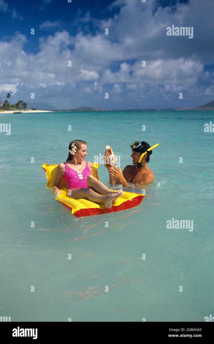 EIN PAAR AUS DEN 1990ER JAHREN, MANN UND FRAU, SCHWIMMEN IM TROPISCHEN  OZEAN MIT FLOSS-SCHNORCHELMASKEN UND FINS, DIE DIE MUSCHELSCHALE  UNTERSUCHEN - KB28018 DEL003 HARS PAAR ROMANTIK SCHÖNHEIT GELBE FARBE INSEL  ALTE