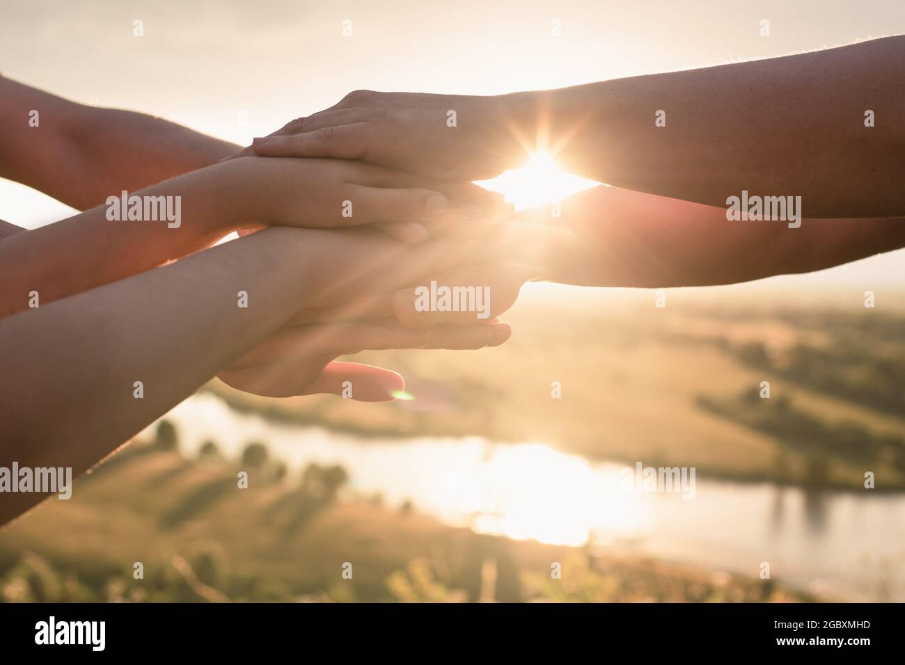 Die Hände der Menschen werden übereinander gefaltet, um das Team zu entwickeln und ein Team vor dem Hintergrund des Himmels und der untergehenden Sonne zu bilden. Der Stockfoto