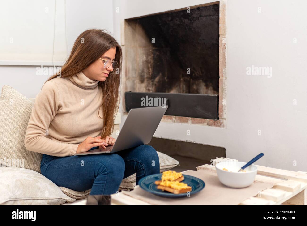 Junge lateinerin, die ihr Mobiltelefon benutzt, während sie zu Hause frühstückt. Stockfoto