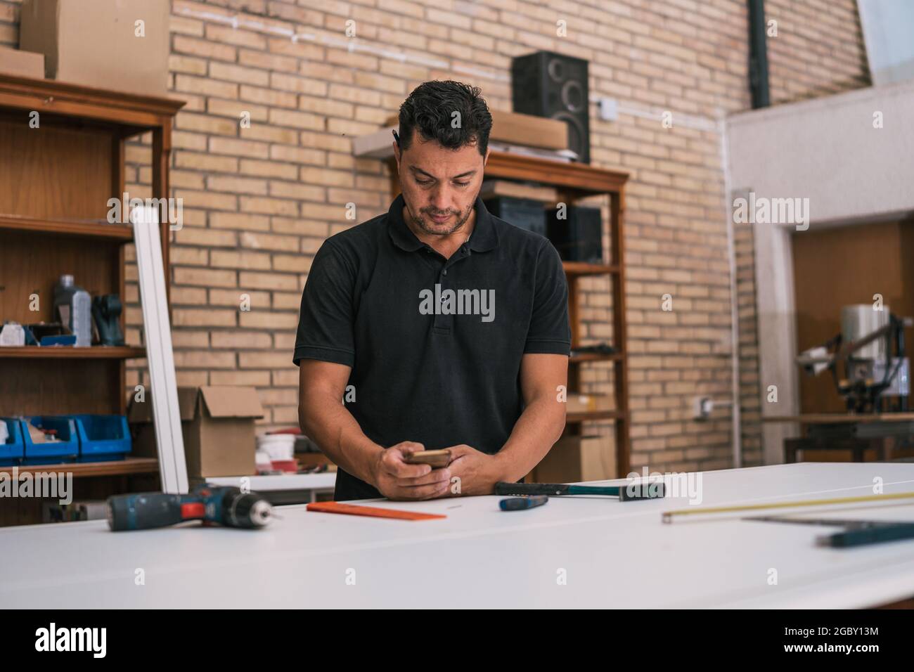 Mann, der in einer Werkstatt ein Smartphone benutzt Stockfoto