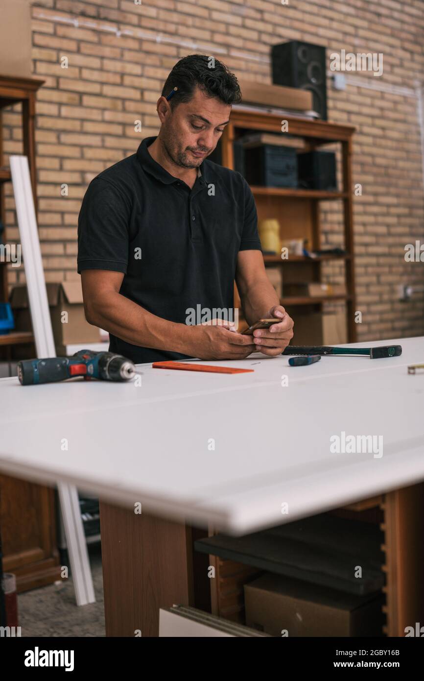 Erwachsener Mann, der in einer Werkstatt ein Mobiltelefon benutzt Stockfoto