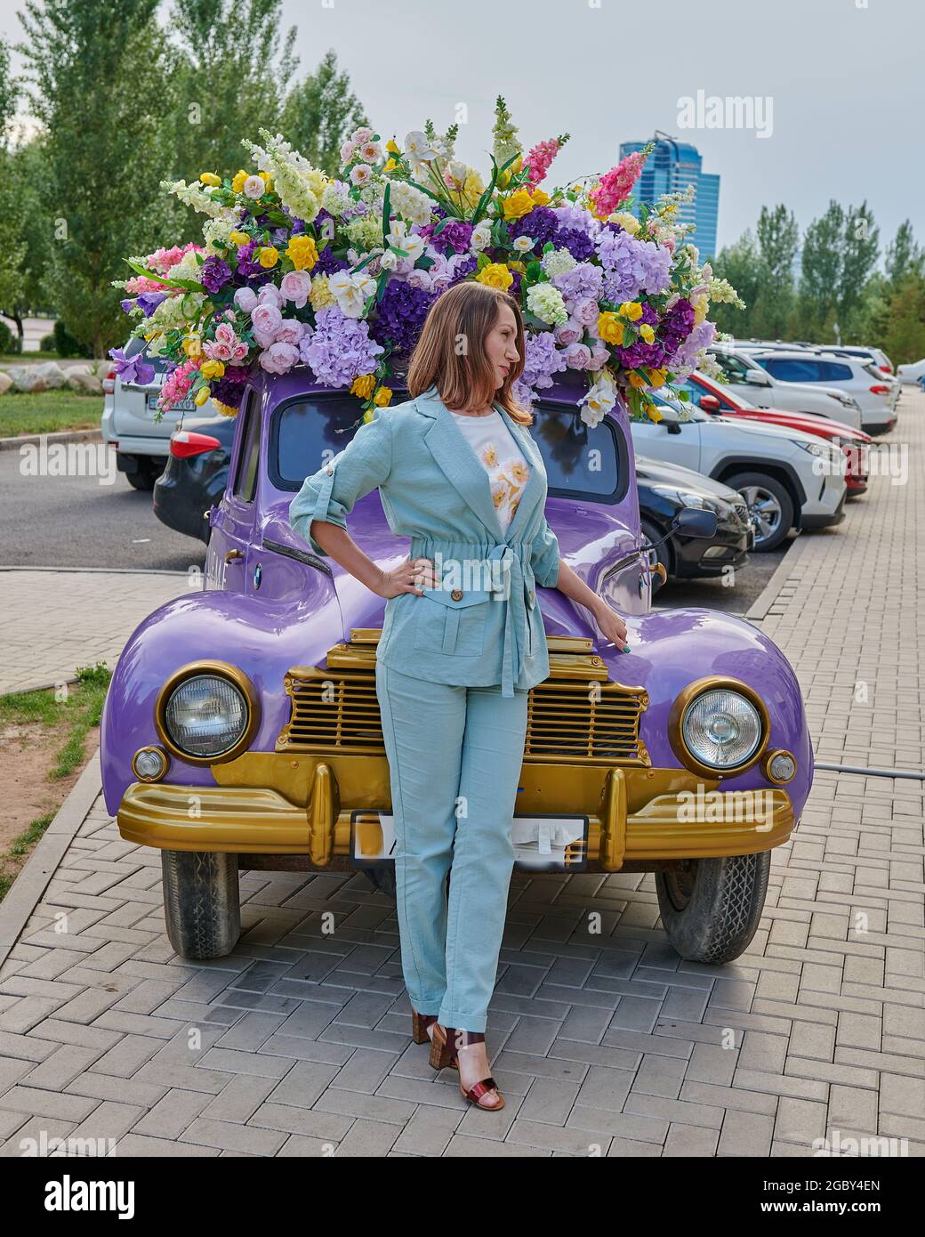 Mädchen in vollem Wachstum auf dem Hintergrund des Autos mit Blumen Stockfoto