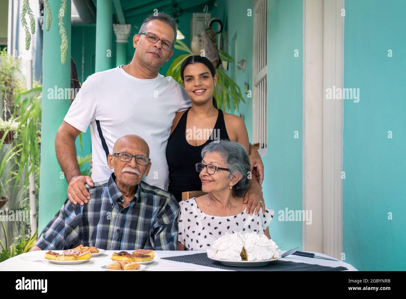Ein älteres Paar mit Brille sitzt an einem Tisch und ein Mann und eine junge Frau stehen hinter den älteren Menschen Stockfoto