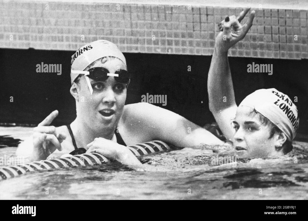Austin, Texas, USA, 1986: Die Schwimmerin der Universität von Texas, Tiffany Cohen, links, und ein Teamkollege blinken am Ende eines Rennens während eines Schwimmtreffens am College auf das Schild mit den Hakenhörnern. ©Bob Daemmrich Stockfoto