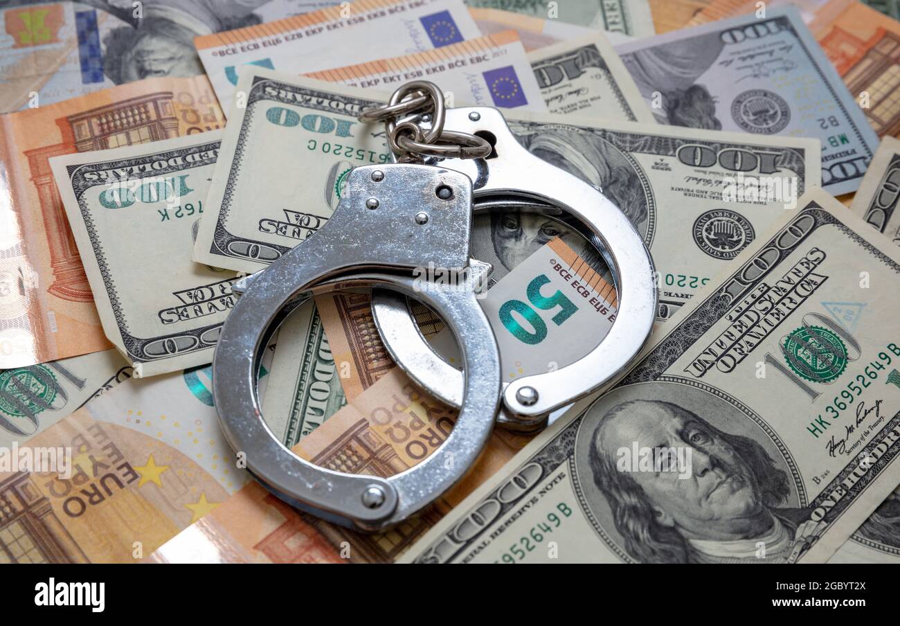 Geld und Verbrechen. Handschellen auf US-Dollar- und Euro-Banknoten im Hintergrund. Bestechung, Korruption und Gerechtigkeit. Stockfoto
