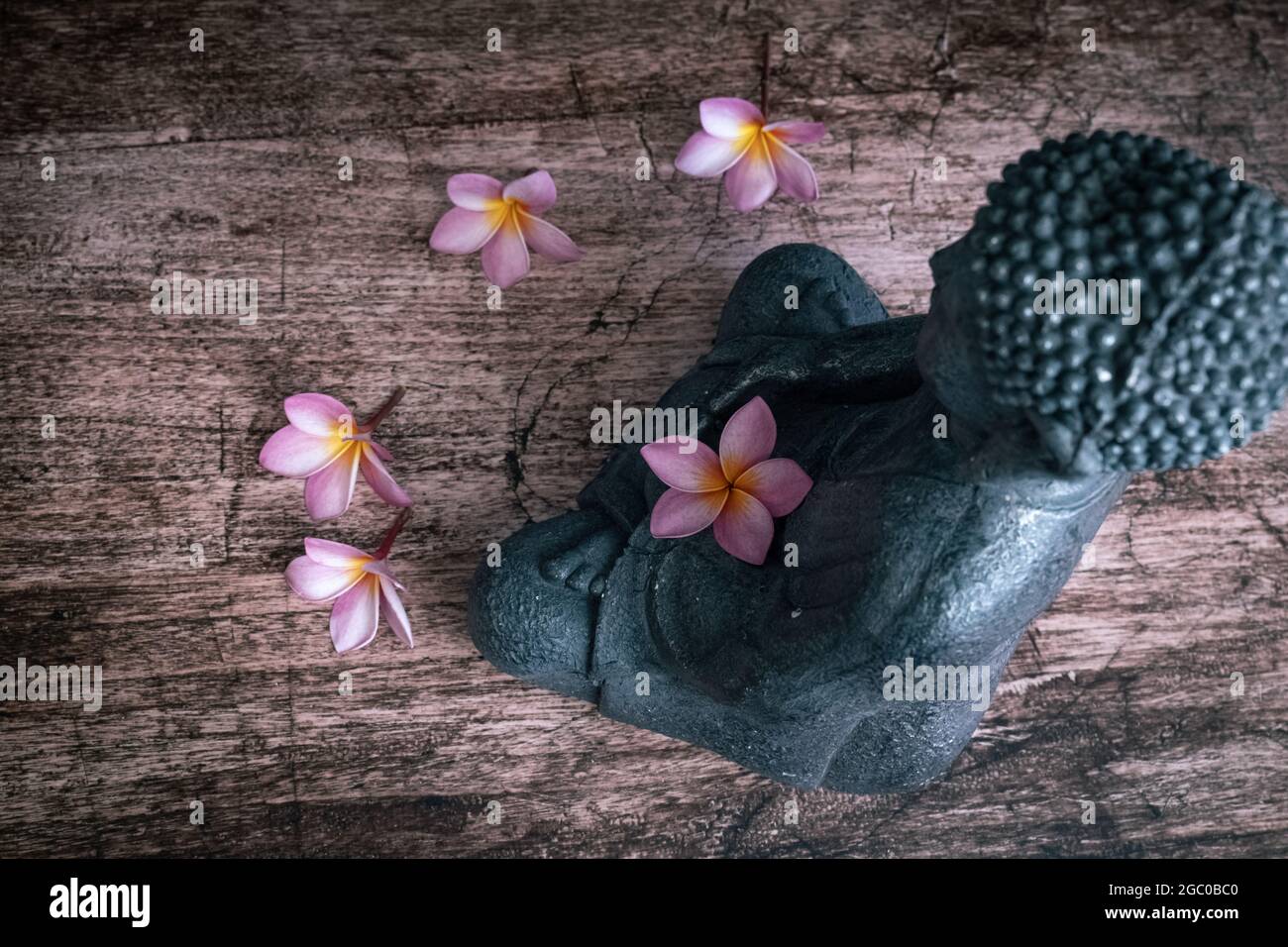 Buddha Statue mit Frangipani Blumen auf einem dunklen Hintergrund Draufsicht Stockfoto