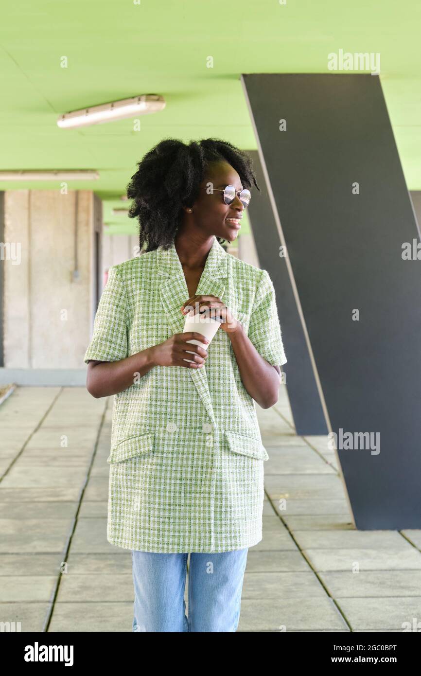 Afrikanische Frau mit einer Tasse Kaffee in einem grünen Jackett und einer Sonnenbrille. Stockfoto