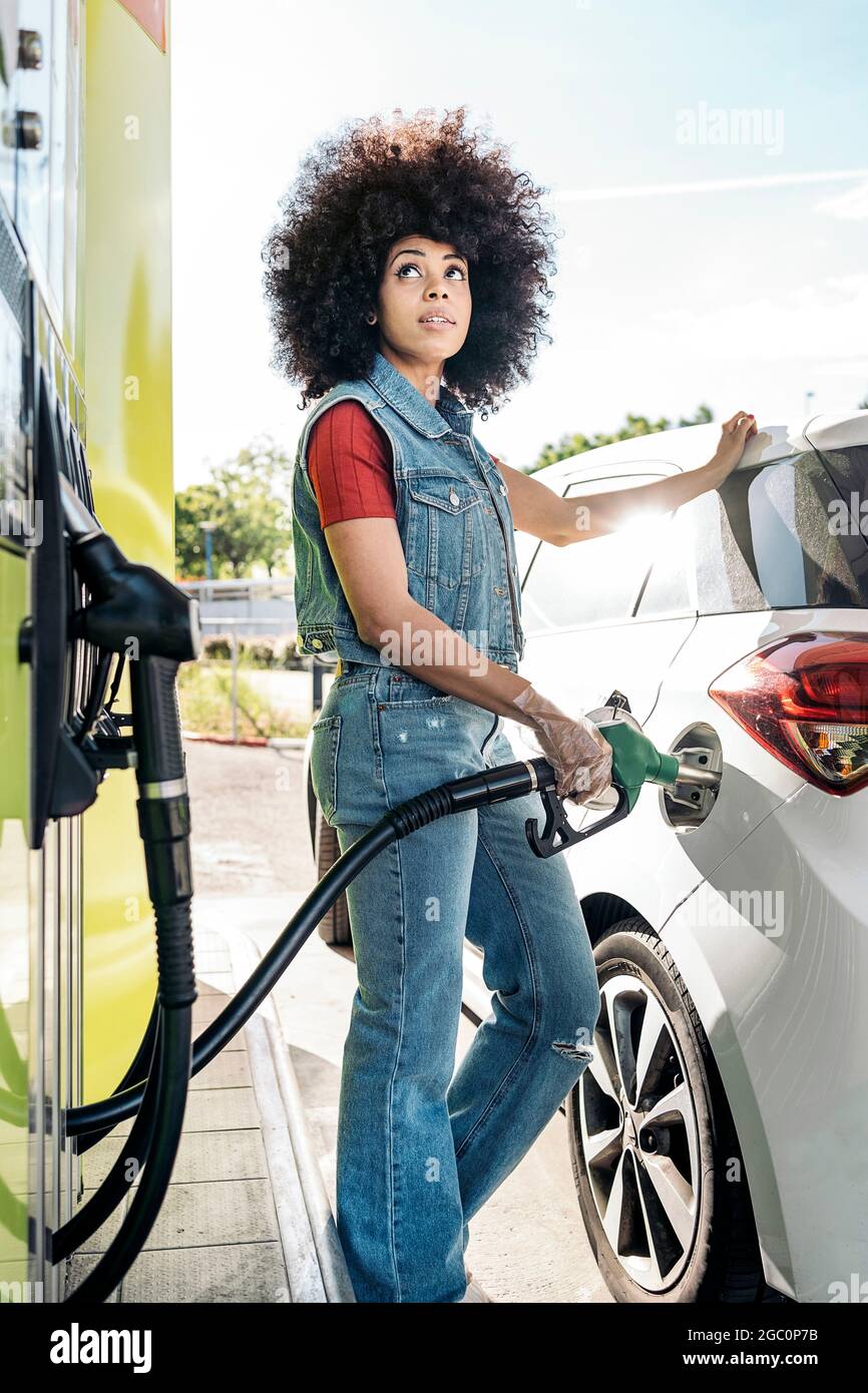 Schöne Frau mit Afro-Haaren, die ihr Auto an der Tankstelle mit Benzin füllte. Stockfoto