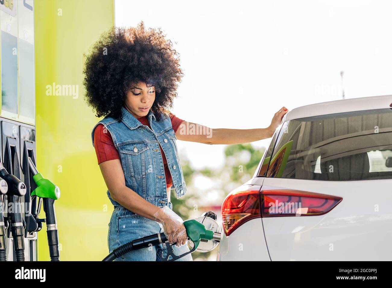 Schöne Frau mit Afro-Haaren, die ihr Auto an der Tankstelle mit Benzin füllte. Stockfoto