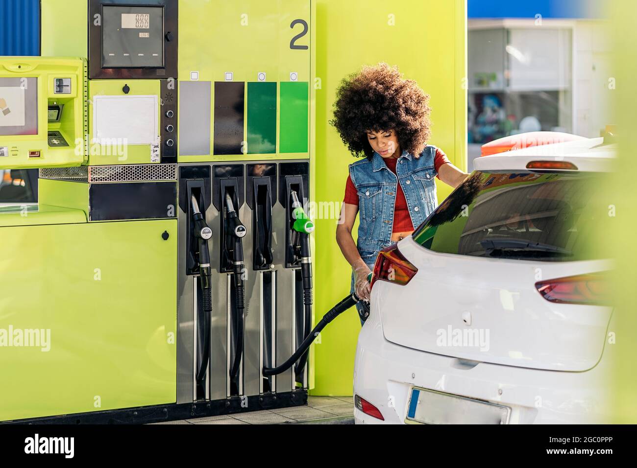 Schöne junge Frau mit Afro-Haaren, die ihr Auto an der Tankstelle mit Benzin füllte. Stockfoto