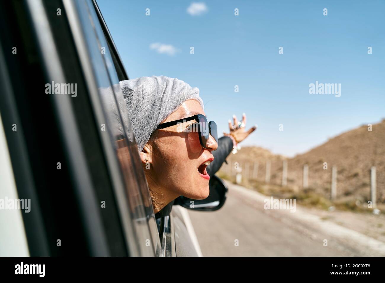 asiatische Frau Touristen, die den Kopf aus der Heckscheibe eines Autos ragt und eine Autoreise genießt Stockfoto