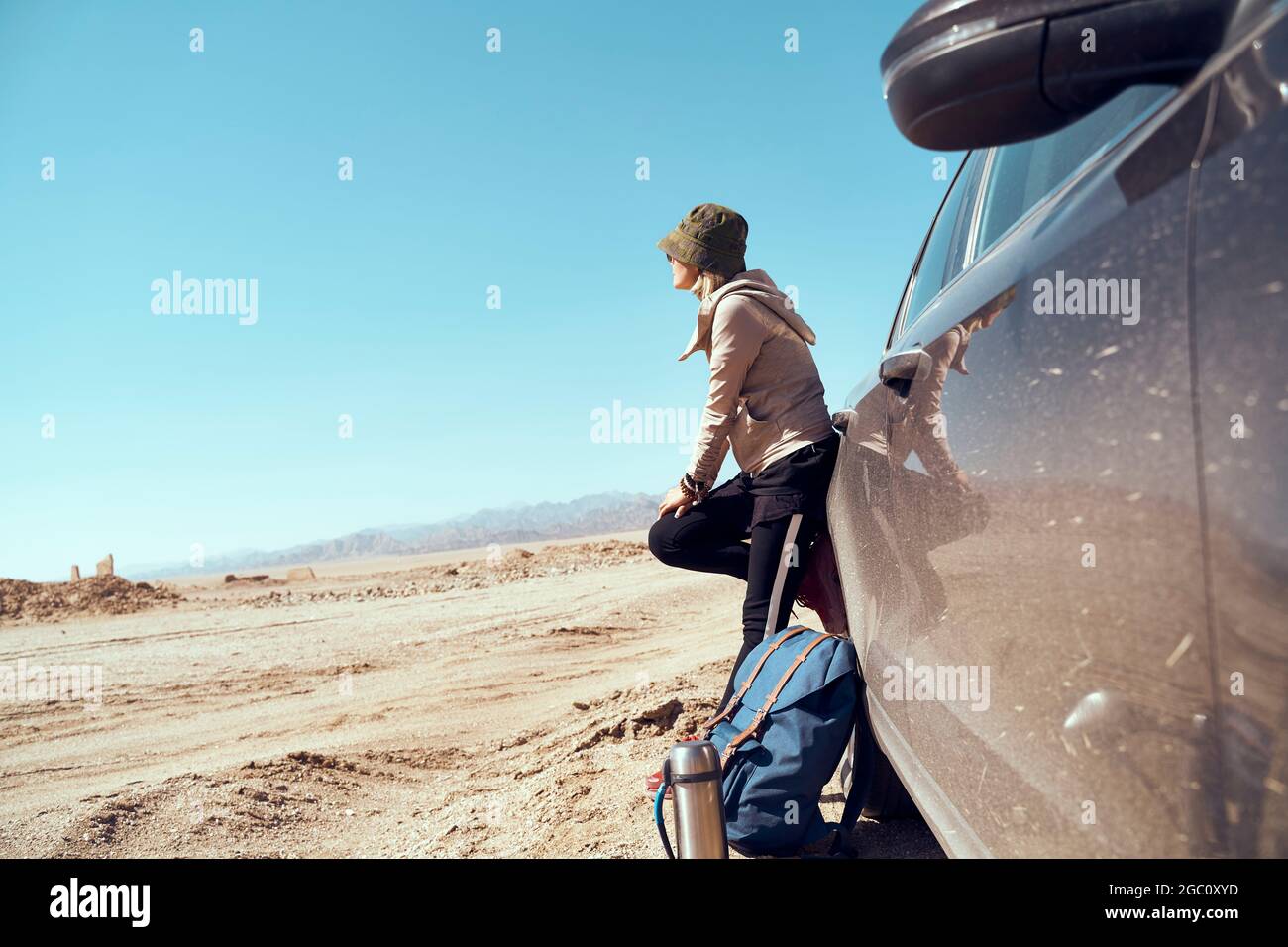 asiatische Frau, die sich gegen das Auto lehnt und die Aussicht in der wüste gobi betrachtet Stockfoto