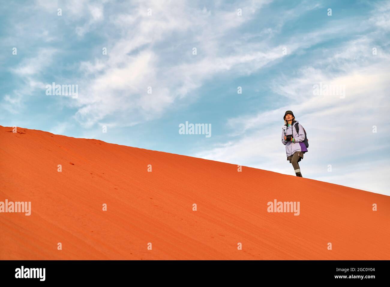 asiatische Fotografin, die auf dem Grat einer Sanddüne läuft und die Aussicht betrachtet Stockfoto