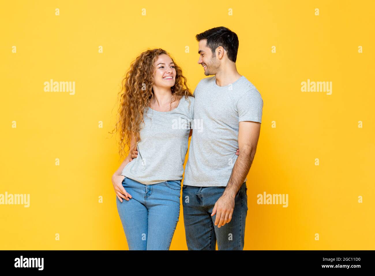 Junge glücklich interracial Millennial Paar hält und suchen einander in den Augen in isolierten gelben Studio Hintergrund Stockfoto