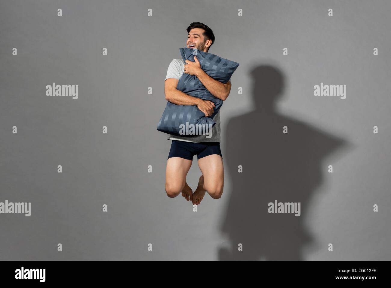 Porträt eines jungen, frisch energischen Mannes, der Schlafanzügen trägt und Kissen hält und in der Luft springt, nachdem er morgens aus einem guten Schlaf im Studio aufgewacht ist Stockfoto