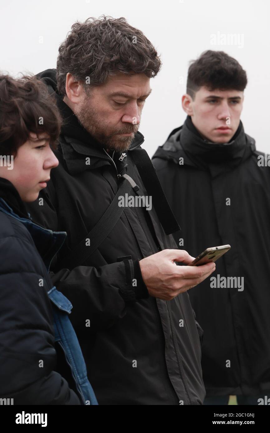 kaukasischer Vater mit Kindern im Teenageralter, die im Winter ein Mobiltelefon halten Stockfoto