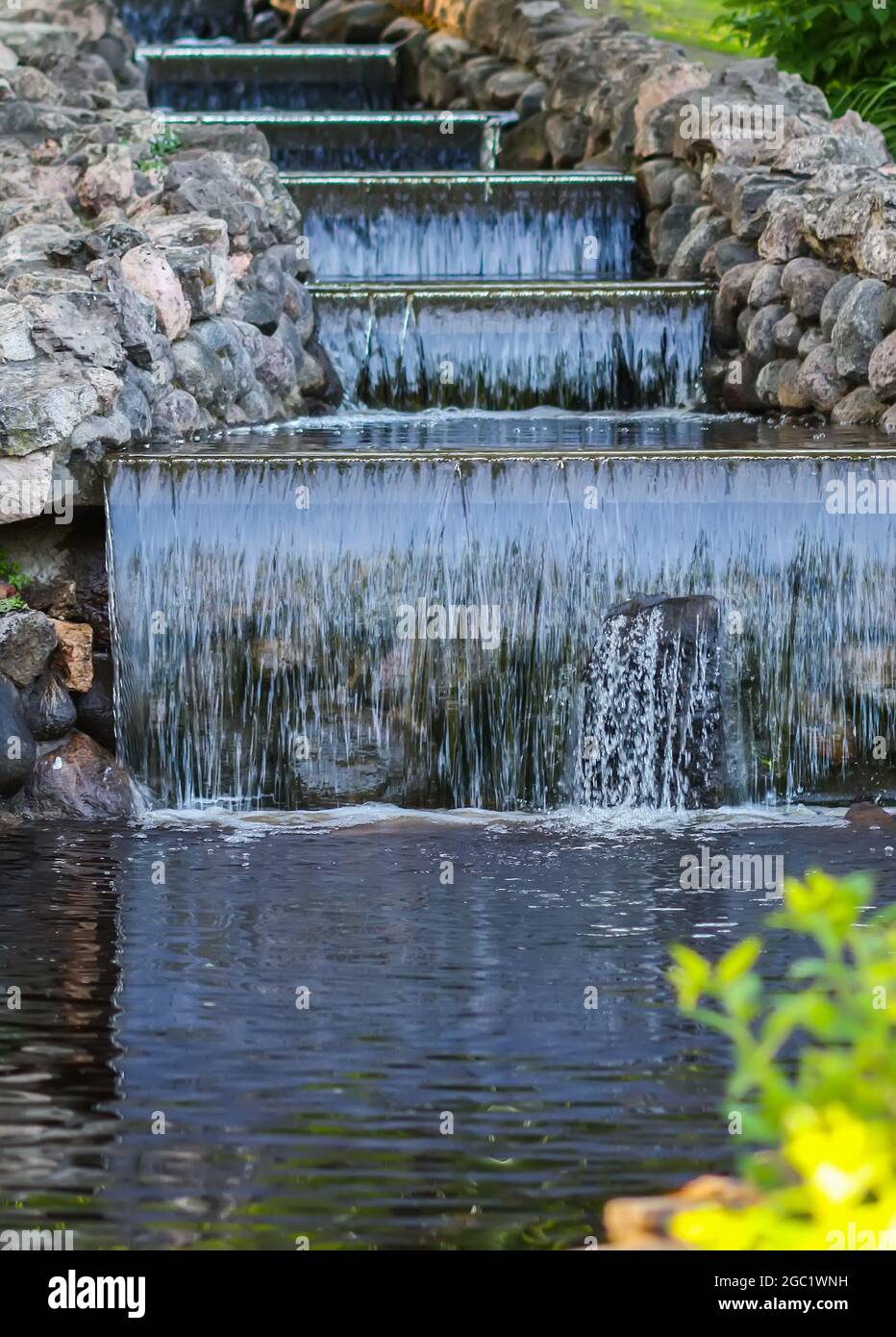 Kaltes transparentes Wasser des dekorativen künstlichen Wasserfalls im Sommerpark. Stockfoto
