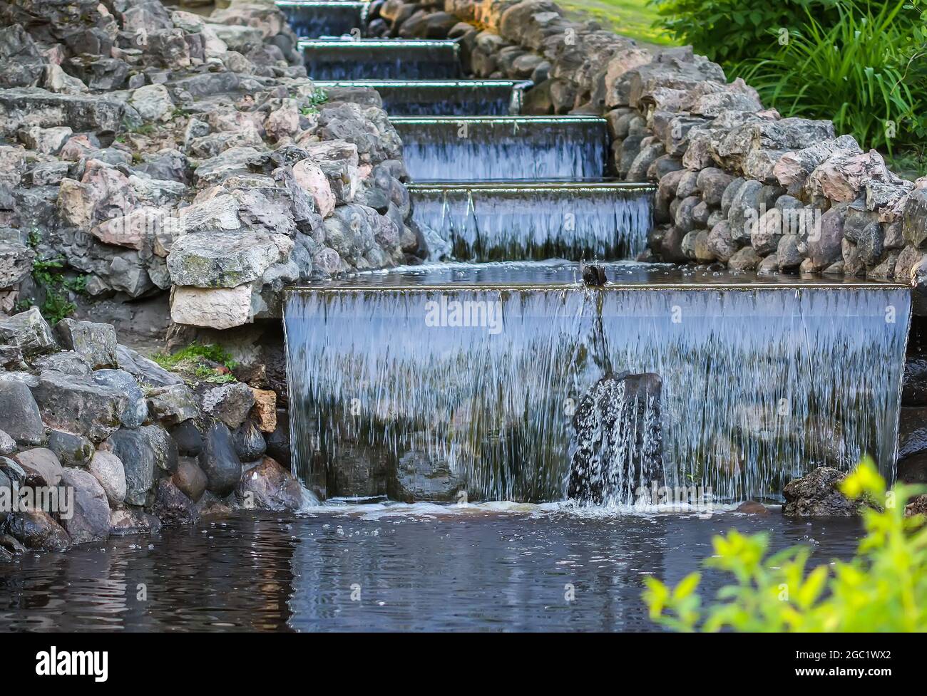 Kaltes transparentes Wasser des dekorativen künstlichen Wasserfalls im Sommerpark. Stockfoto