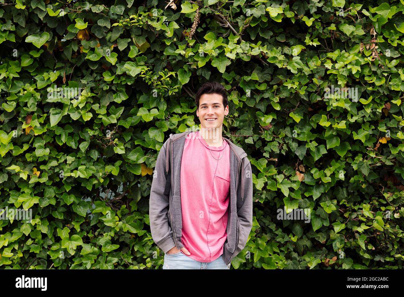 Freundlicher, lächelnder Teenager, der auf einem grünen Pflanzenhintergrund die Kamera anschaut, Konzept menschlicher Ausdrücke und Emotionen, Platz für Text kopieren Stockfoto