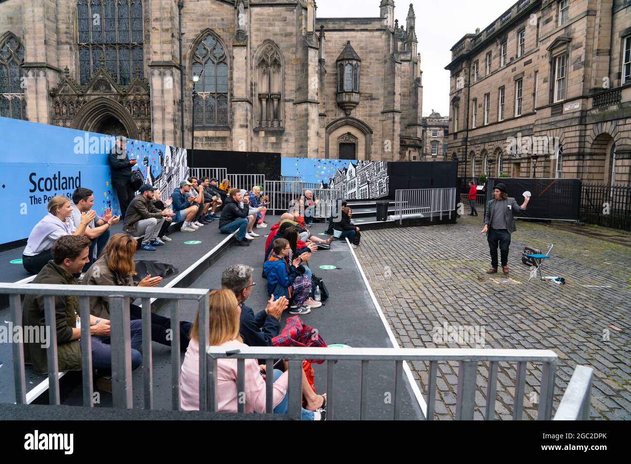 Edinburgh, Schottland, Großbritannien. August 2021. Bilder von der Royal Mile in der Altstadt von Edinburgh am Eröffnungstag des Edinburgh Fringe Festivals 2021. Das Festival sieht ganz anders aus als vor zwei Jahren. Nur sehr wenige Straßenaufführungsräume sind erlaubt und deutlich weniger Touristen sind zu sehen. Auch eine hohe Sichtbarkeit der Polizei, es gibt mehr Polizeibeamte als Darsteller auf der Straße, steht in einem deutlichen Kontrast zu den Vorjahren. PIC; Performer unterhält die Menge in speziell dafür eingerichteten, abgeschirmten Veranstaltungsräumen im Freien, die die Kapazität des Publikums einschränken. Iain Masterton/Alamy Live Nachrichten. Stockfoto