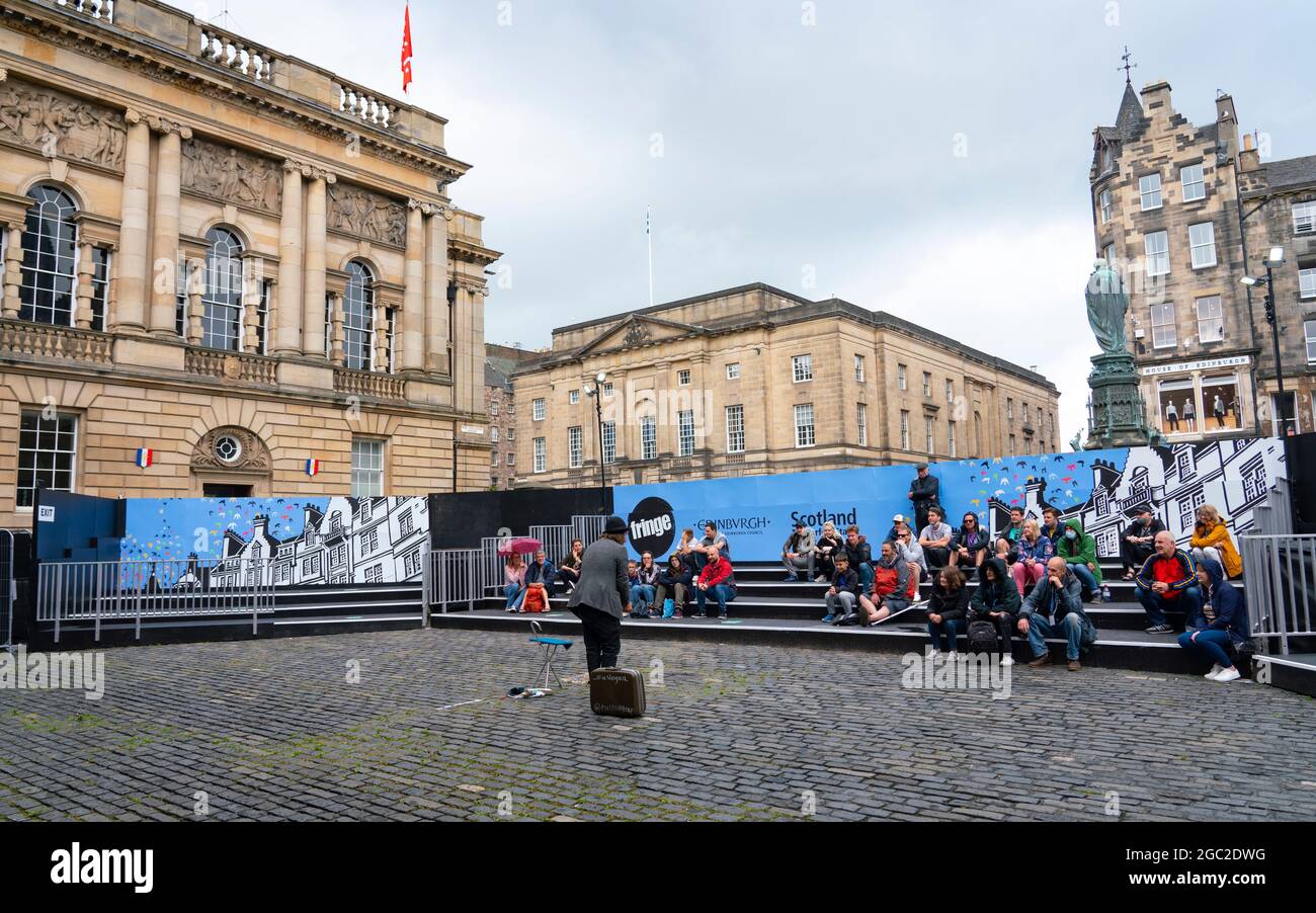 Edinburgh, Schottland, Großbritannien. August 2021. Bilder von der Royal Mile in der Altstadt von Edinburgh am Eröffnungstag des Edinburgh Fringe Festivals 2021. Das Festival sieht ganz anders aus als vor zwei Jahren. Nur sehr wenige Straßenaufführungsräume sind erlaubt und deutlich weniger Touristen sind zu sehen. Auch eine hohe Sichtbarkeit der Polizei, es gibt mehr Polizeibeamte als Darsteller auf der Straße, steht in einem deutlichen Kontrast zu den Vorjahren. PIC; Performer unterhält die Menge in speziell dafür eingerichteten, abgeschirmten Veranstaltungsräumen im Freien, die die Kapazität des Publikums einschränken. Iain Masterton/Alamy Live Nachrichten. Stockfoto