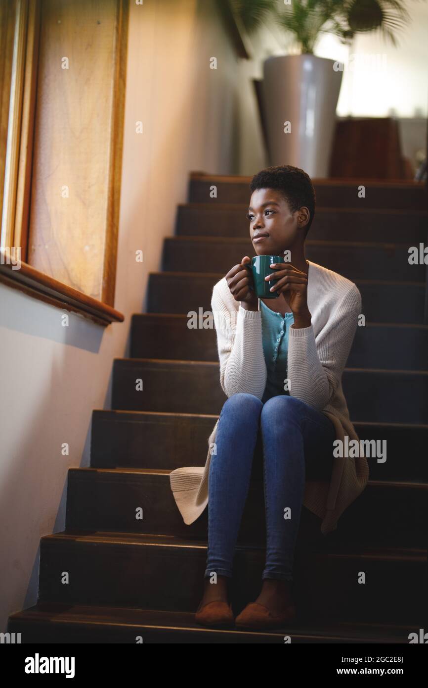 Lächelnde afroamerikanische Frau, die auf einer Treppe sitzt und Kaffee trinkt Stockfoto