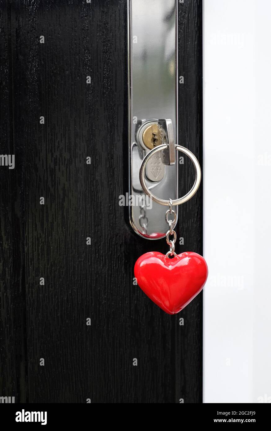 Hausschlüssel auf rotem herzförmigem Schlüsselanhänger im Türschloss Stockfoto