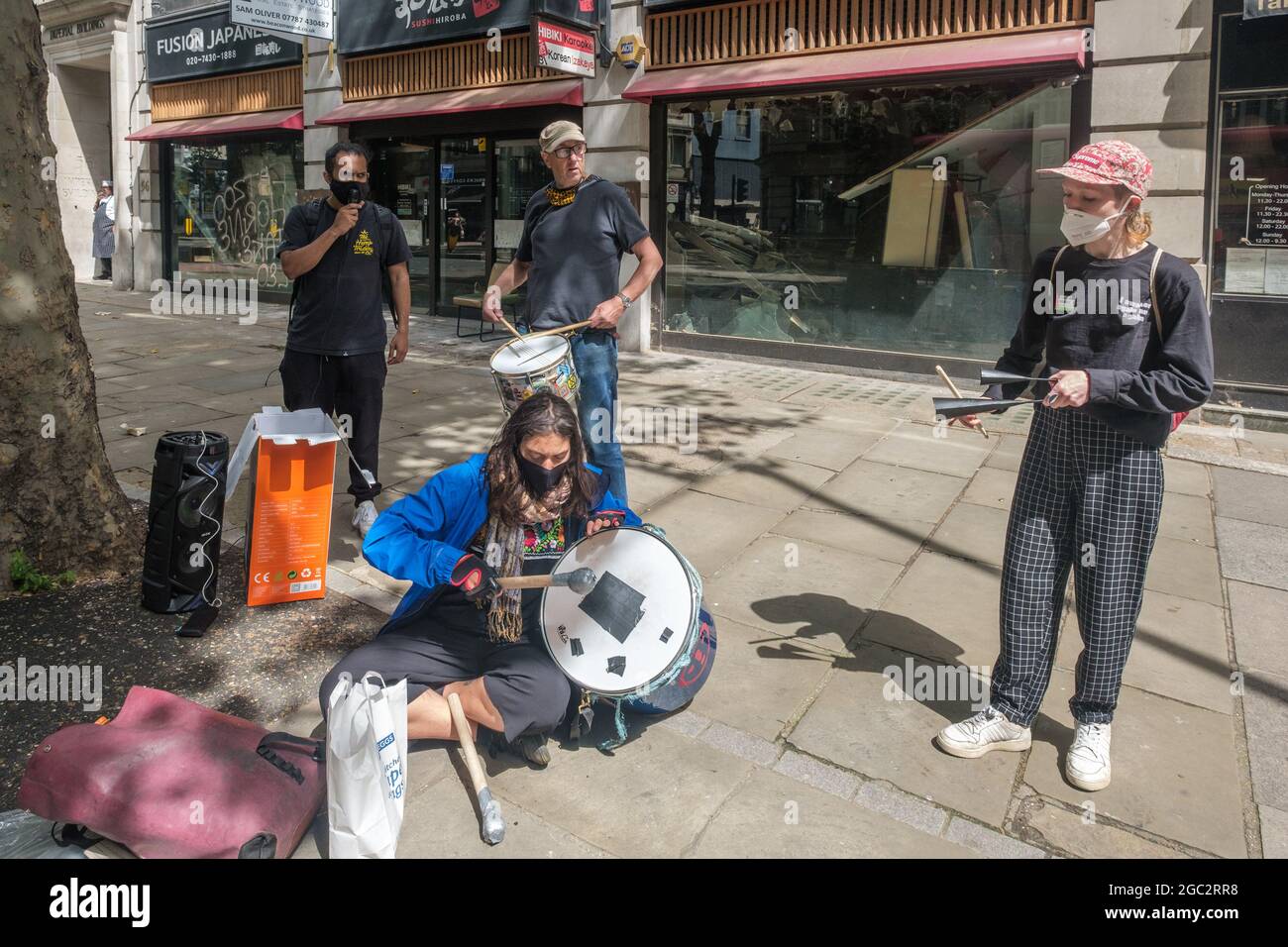 London, Großbritannien. August 2021. Zwei Demonstranten der Palestine Action sitzen mit Spruchbändern auf der Kante im ersten Stock über dem Eingang zu den Londoner Büros des israelischen Waffenherstellers Elbit Systems in Kingsway, mit Spruchbändern und gemalten Botschaften "Elbit tötet", "Shut Elbit Down". Elbit liefert Waffen an die israelische Regierung, um Kriegsverbrechen in Gaza zu begehen, und vermarktet ihre Waffen als "kampferprobt" wegen ihres Einsatzes gegen Palästinenser. Andere spielten Trommeln auf der gegenüberliegenden Straßenseite, um auf den Protest aufmerksam zu machen. Peter Marshall/Alamy Live News Stockfoto