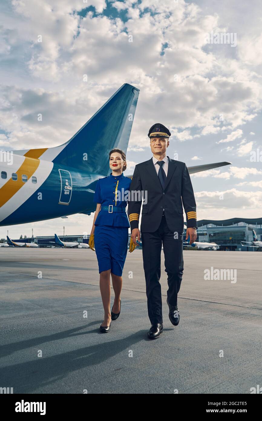 Lächelnde weibliche Flugbegleiterin und ein Flugzeugpilot, der vor uns hergeht Stockfoto