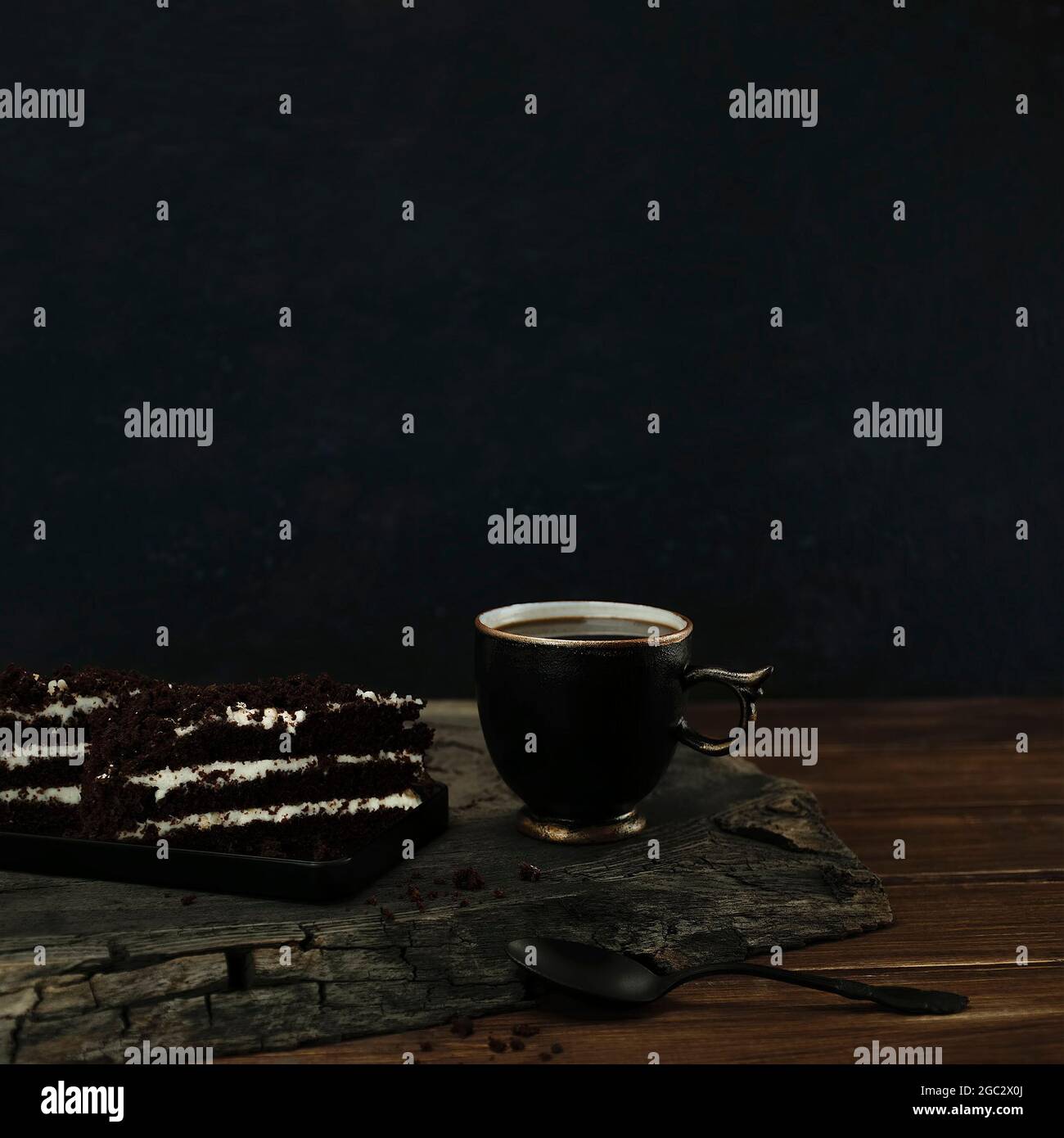 Tasse schwarzen Kaffee mit Stücken Schokoladenkuchen und Löffel auf einem hölzernen geknackten Eichenschnitt. Draufsicht mit Kopierbereich von dunkelblauem Bokeh-Hintergrund Stockfoto