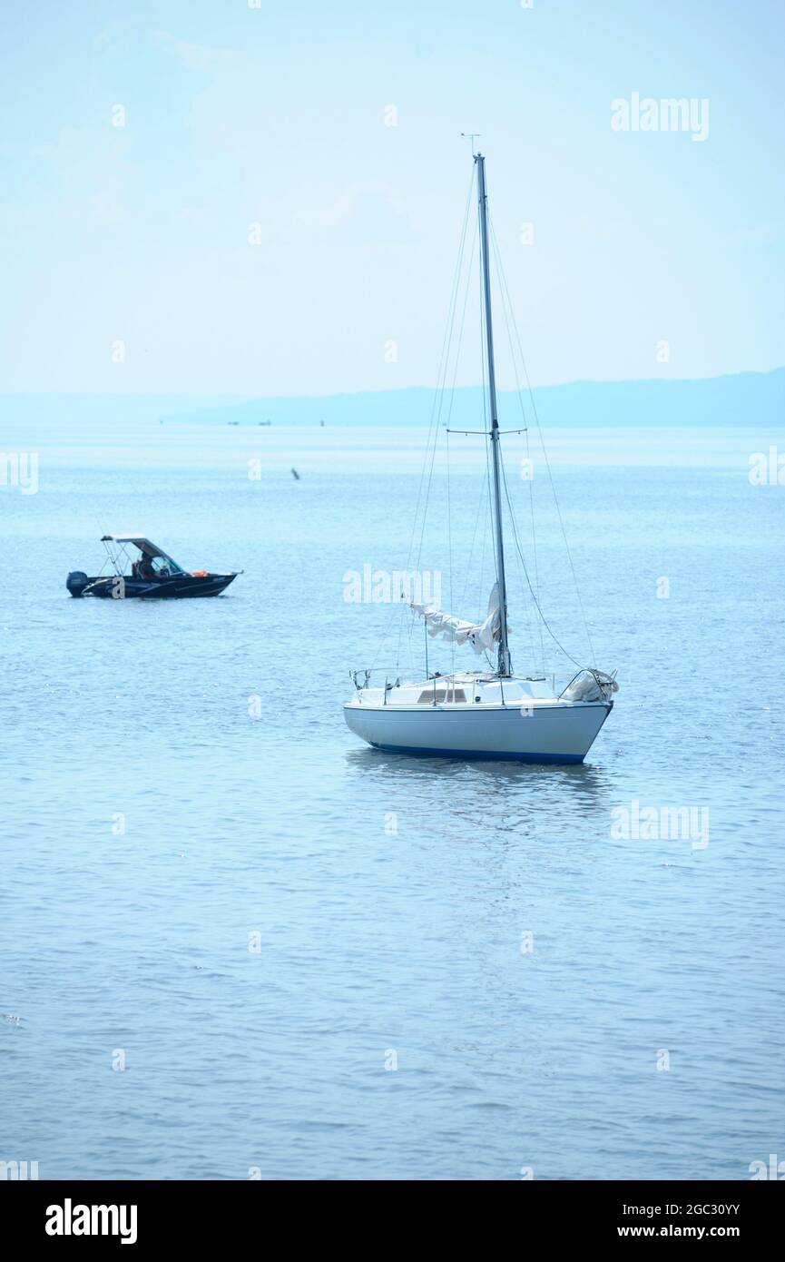 Segelyacht-Fahrt vor Anker in der Bucht, nebeliges Ufer in der Ferne sichtbar Stockfoto