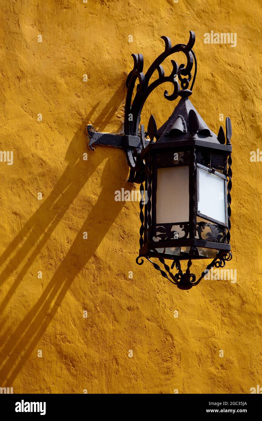 Verzierte Straßenlampe aus schwarzem Metall an einer gelben Waschwand in Cartagena, Kolumbien. Stockfoto