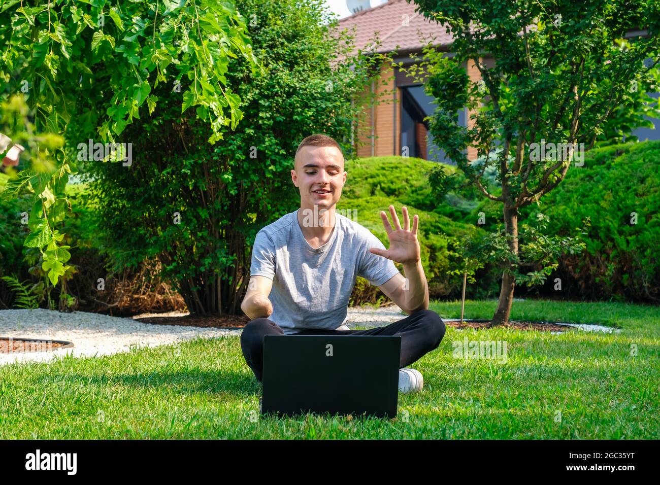 Kerl mit amputierten Arm sitzt auf dem Rasen und im Gespräch mit Freunden über soziales Netzwerk Stockfoto