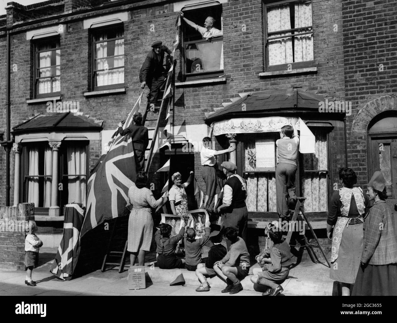 Die Menschen der Kimpton Road, die ihre Krönungsdekorationen heute Nachmittag aufsetzen, werden von den Kiddies beobachtet, die sich sicherlich auf ihre Party freuen, die die Menschen der Kimpton Road ihnen am Krönungstag (Queen Elizabeth II) 1953 geben. Stockfoto