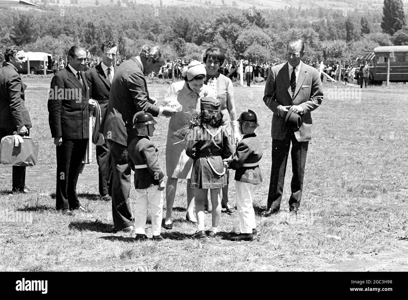 Pucon, Chile: Drei einheimische Kinder (zwei Jungen und ein Mädchen), die sich als Feuerwehrmaskotten kleiden, präsentieren Königin Elizabeth II. Hier am 15. November einen Blumenstrauß. Den Blumenstrauß von den Kindern nimmt Außenminister Valdes. Die Königin, die von Prinz Philip (ganz rechts) akkommaiert wurde, ist auf einem 8-tägigen Staatsbesuch in Chile. 19. November 1968 Stockfoto